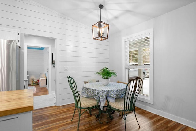 dining room with lofted ceiling, dark hardwood / wood-style floors, wood walls, and an inviting chandelier