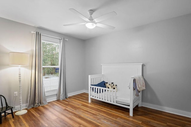 bedroom with hardwood / wood-style floors, a crib, and ceiling fan