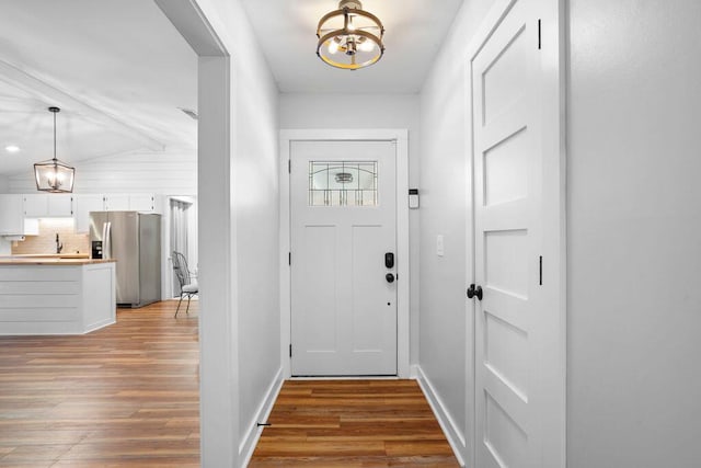 doorway to outside with a notable chandelier, lofted ceiling with beams, and light wood-type flooring