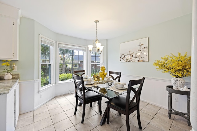 dining area featuring an inviting chandelier, wainscoting, and light tile patterned floors