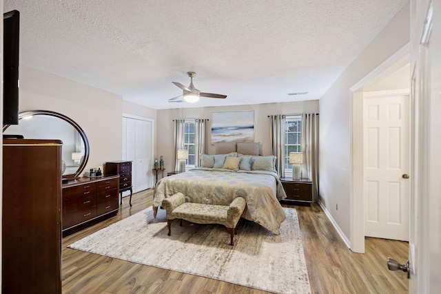 bedroom featuring a closet, baseboards, light wood-type flooring, a textured ceiling, and a ceiling fan