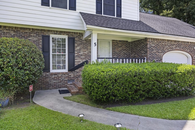entrance to property with an attached garage, a shingled roof, and brick siding