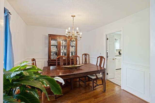 dining space with light wood-style flooring, a decorative wall, a notable chandelier, and wainscoting