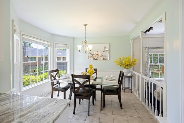 dining room with light tile patterned floors, a wealth of natural light, a chandelier, and a wainscoted wall