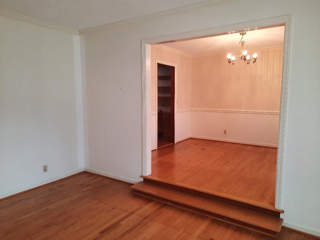 spare room featuring a notable chandelier, crown molding, and wood finished floors