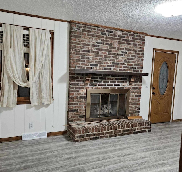 unfurnished living room with visible vents, ornamental molding, a textured ceiling, wood finished floors, and a fireplace