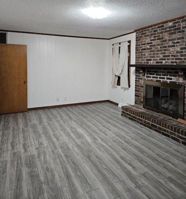 unfurnished living room with a fireplace, a textured ceiling, wood finished floors, and crown molding