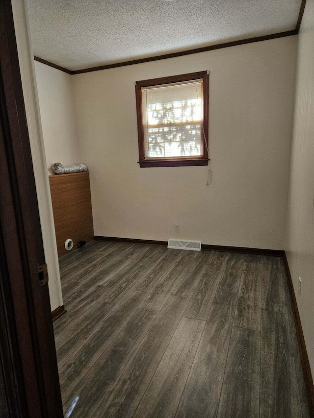 spare room featuring visible vents, ornamental molding, a textured ceiling, dark wood-style floors, and baseboards