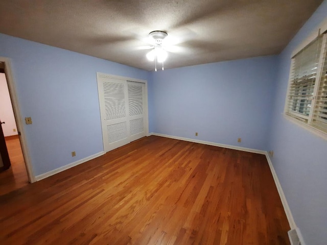 unfurnished bedroom featuring wood finished floors, baseboards, ceiling fan, a closet, and a textured ceiling