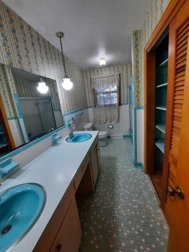 full bathroom with wallpapered walls, a shower stall, a wainscoted wall, and a sink