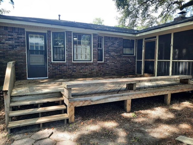 rear view of house featuring brick siding, a deck, and a sunroom