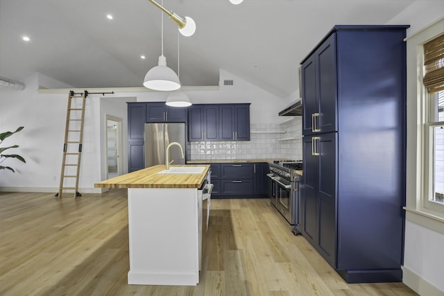 kitchen with a barn door, butcher block countertops, decorative backsplash, a center island with sink, and appliances with stainless steel finishes