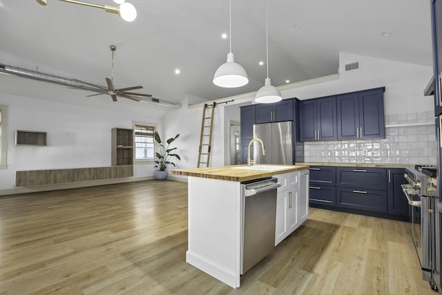 kitchen featuring wood counters, appliances with stainless steel finishes, a barn door, lofted ceiling, and an island with sink