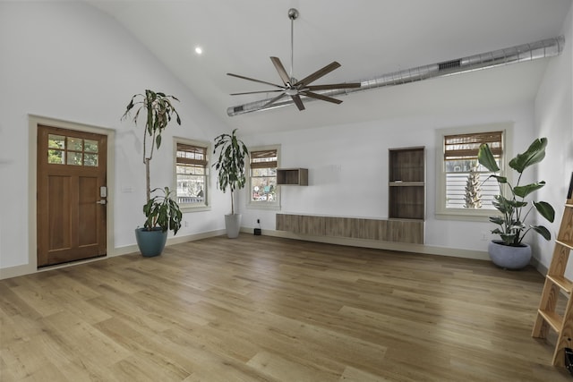 unfurnished living room with ceiling fan, a healthy amount of sunlight, light wood-type flooring, and vaulted ceiling