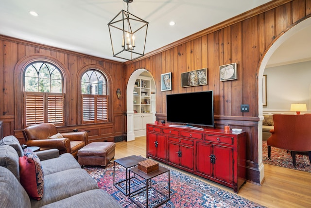 living room with light hardwood / wood-style floors, built in features, wood walls, ornamental molding, and a chandelier