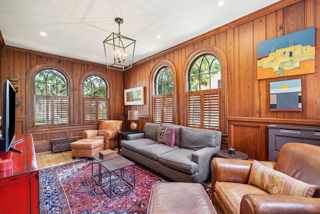 living room with hardwood / wood-style flooring, crown molding, a notable chandelier, and wooden walls