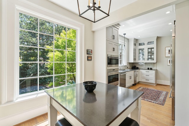 kitchen with an inviting chandelier, white cabinetry, light hardwood / wood-style floors, tasteful backsplash, and pendant lighting