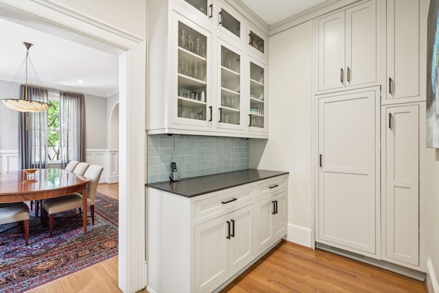 kitchen featuring decorative light fixtures, decorative backsplash, crown molding, light hardwood / wood-style flooring, and white cabinets