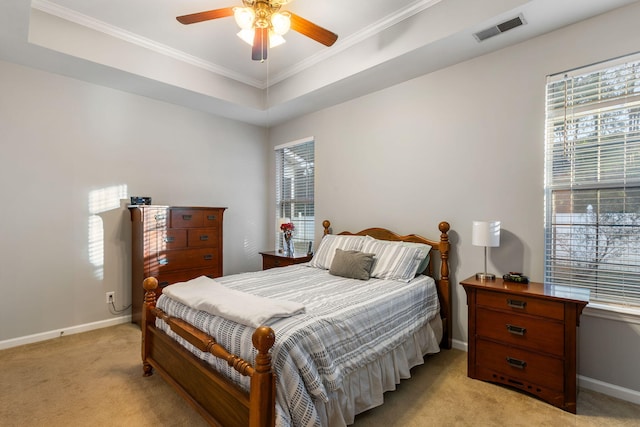 carpeted bedroom with a raised ceiling, multiple windows, ceiling fan, and ornamental molding