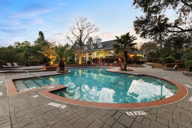 pool at dusk featuring a patio and a community pool