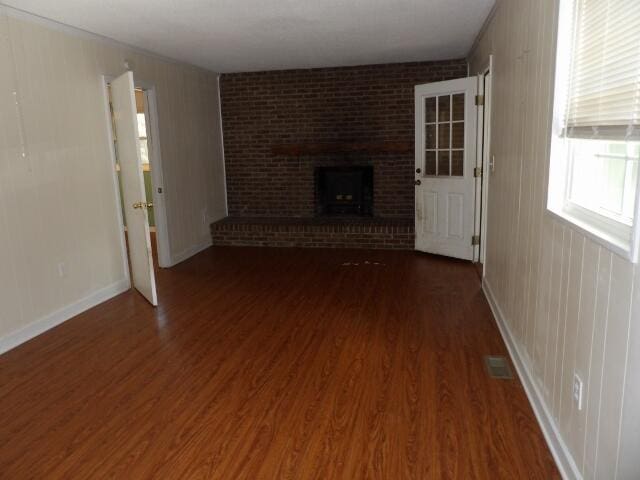 unfurnished living room with a brick fireplace and dark hardwood / wood-style floors