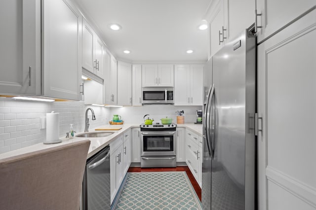 kitchen featuring appliances with stainless steel finishes, dark wood-type flooring, white cabinetry, decorative backsplash, and sink