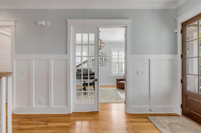 interior space with a wainscoted wall, ornamental molding, light wood-style flooring, and a decorative wall