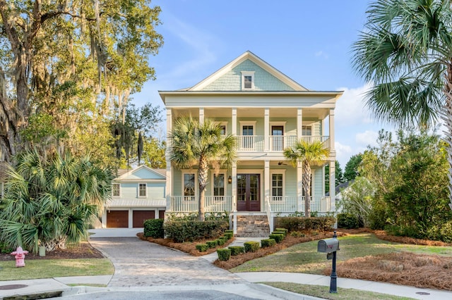 view of front facade featuring a porch, an attached garage, a balcony, french doors, and decorative driveway