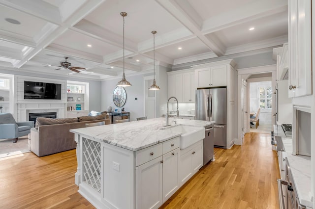 kitchen with light wood-style flooring, appliances with stainless steel finishes, a glass covered fireplace, white cabinetry, and a sink