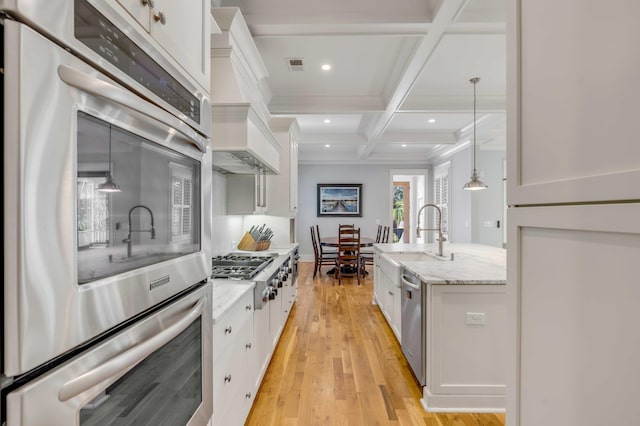 kitchen featuring light wood finished floors, visible vents, coffered ceiling, stainless steel appliances, and a sink