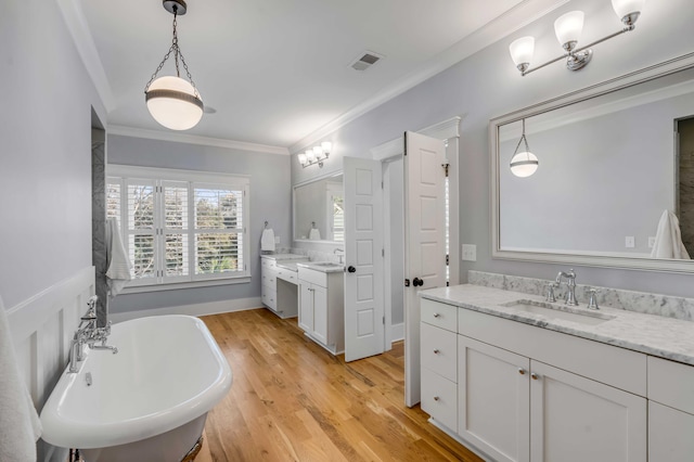 full bath with crown molding, two vanities, a sink, wood finished floors, and a freestanding tub