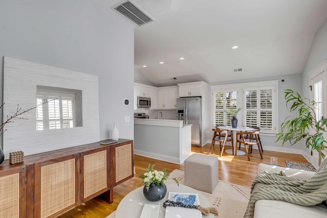 living room featuring lofted ceiling, light wood-style flooring, visible vents, and recessed lighting