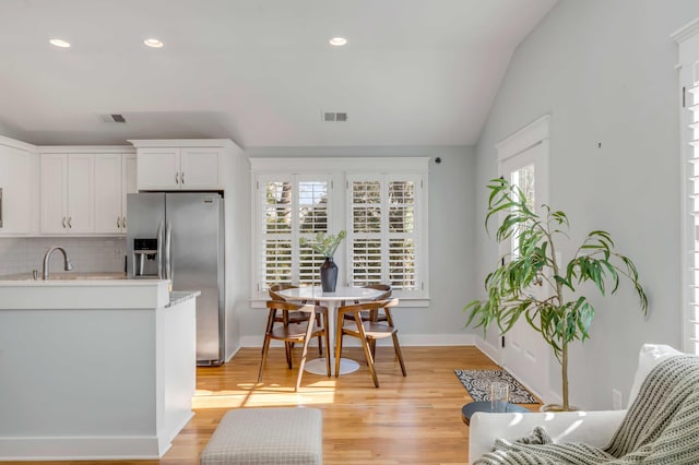 kitchen with visible vents, light countertops, stainless steel refrigerator with ice dispenser, backsplash, and light wood finished floors