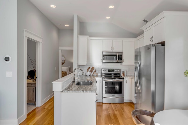 kitchen with stainless steel appliances, white cabinetry, a sink, and a peninsula