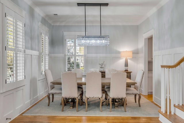 dining area with a decorative wall, wood finished floors, a wealth of natural light, and a notable chandelier