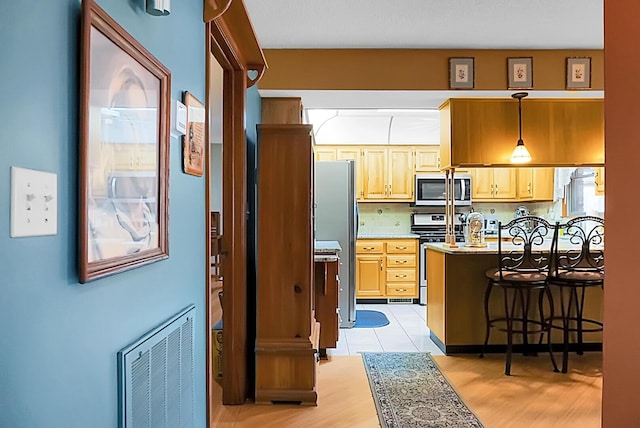 kitchen with a breakfast bar area, appliances with stainless steel finishes, hanging light fixtures, backsplash, and light brown cabinetry