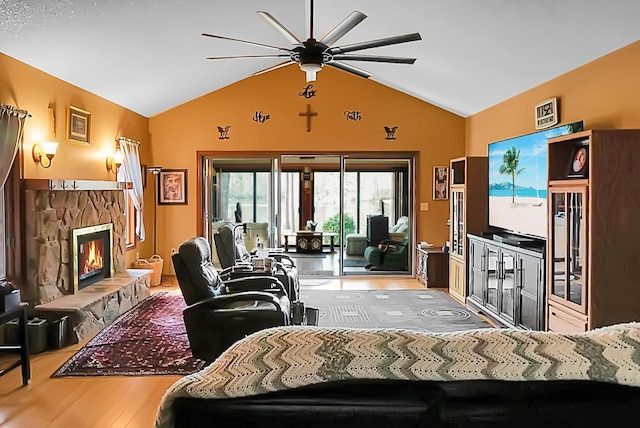 living room featuring ceiling fan, lofted ceiling, wood-type flooring, and a stone fireplace