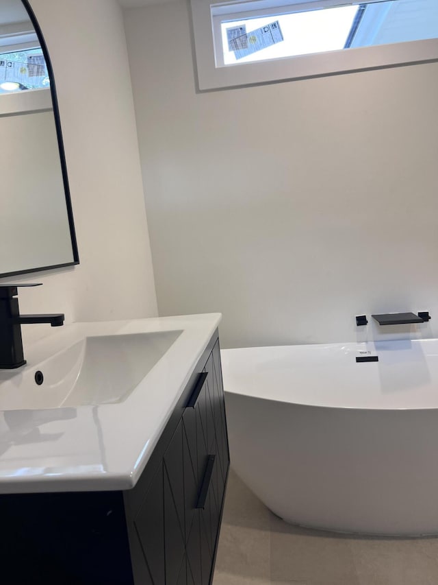full bathroom with tile patterned flooring, a healthy amount of sunlight, a freestanding bath, and vanity