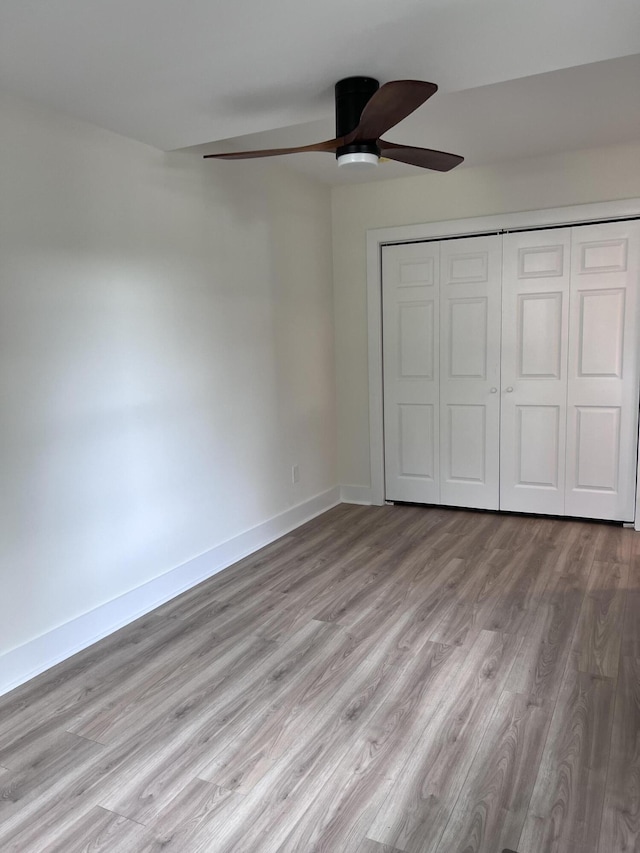 unfurnished bedroom featuring a closet, baseboards, wood finished floors, and a ceiling fan