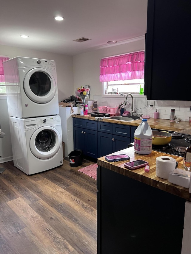 laundry room with wood finished floors, visible vents, laundry area, a sink, and stacked washer / drying machine