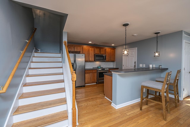 kitchen with pendant lighting, appliances with stainless steel finishes, a kitchen breakfast bar, kitchen peninsula, and light wood-type flooring