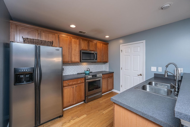 kitchen with sink, decorative backsplash, light wood-type flooring, and appliances with stainless steel finishes