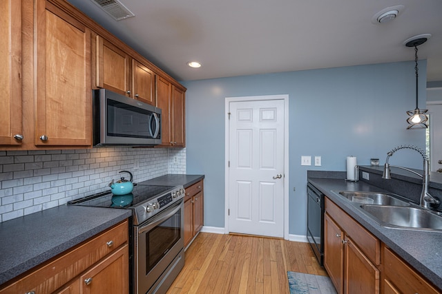 kitchen featuring sink, light hardwood / wood-style flooring, hanging light fixtures, stainless steel appliances, and tasteful backsplash