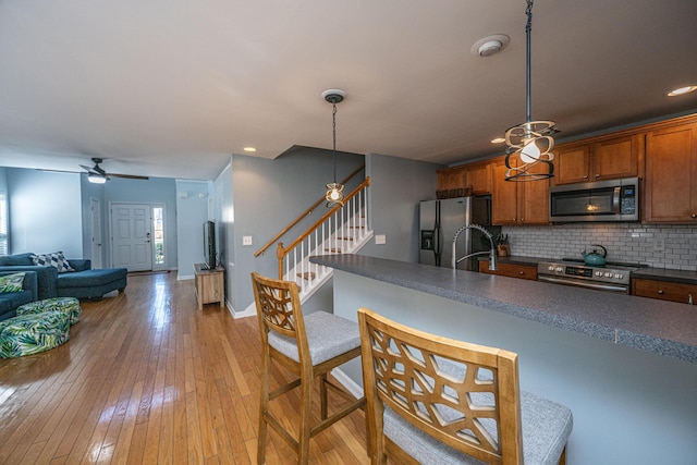 kitchen with pendant lighting, sink, stainless steel appliances, tasteful backsplash, and light wood-type flooring