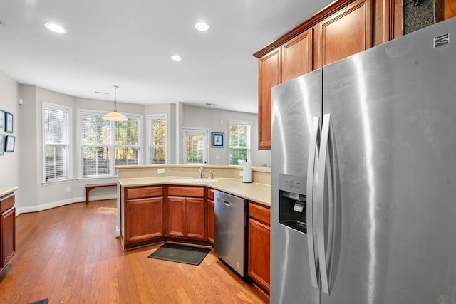 kitchen featuring pendant lighting, sink, light hardwood / wood-style floors, kitchen peninsula, and stainless steel appliances