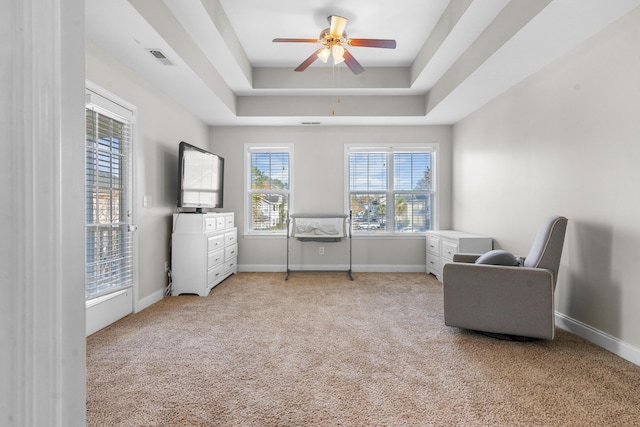 living area featuring ceiling fan, light colored carpet, and a tray ceiling