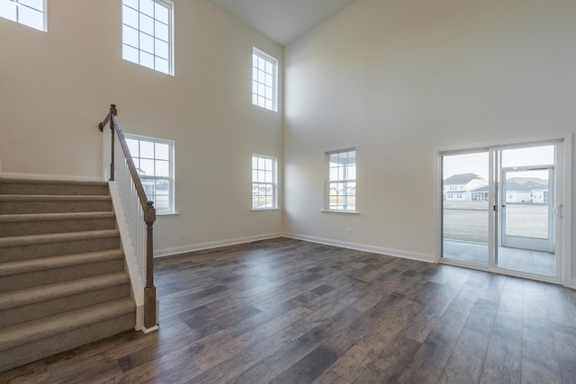 unfurnished living room featuring dark wood-type flooring and a towering ceiling