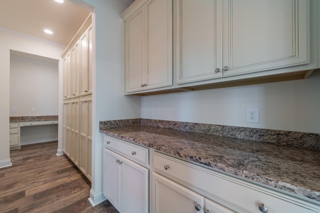 kitchen with dark wood-type flooring, white cabinets, built in desk, and dark stone countertops