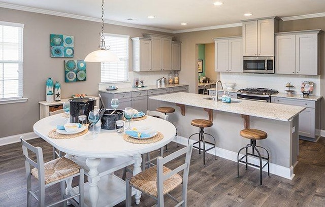 kitchen featuring stainless steel appliances, crown molding, hanging light fixtures, and a center island with sink