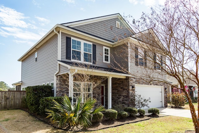 view of front of house with stone siding, an attached garage, driveway, and fence